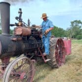 Man in overalls standing on steam tractor.