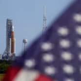 An American flag flies in front of a NASA moon rocket.