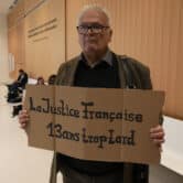 A man holds a placard reading "The French justice, 13 years too late" in a Paris courthouse.