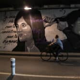 A woman rides a bicycle in front of a mural depicting women cutting their hair.
