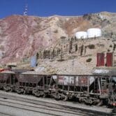 Rusty railcars with a mountain behind.