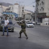 An Israeli soldier draws his weapon on Palestinians.