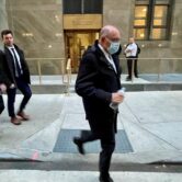 Former Trump Organization CFO Allen Weisselberg is walking on the sidewalk outside of Manhattan Criminal Court, he is wearing a black suit, two other men in suits are walking behind him
