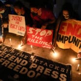 Activists light candles beside slogans as they condemn the killing of Filipino journalist.