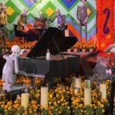 A skeleton plays the piano surrounded by marigold flowers