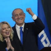Benjamin Netanyahu hugs his wife Sara while gesturing behind a lectern.
