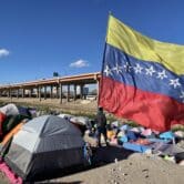 A migrant from Venezuela looks out from under a large Venezuelan flag
