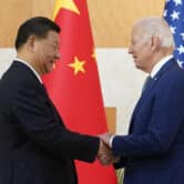 Xi Jinping and Joe Biden shake hands in front of Chinese and American flags.