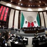 Federal legislators face the dais, Mexican flags and vote count in Mexico’s Chamber of Deputies