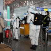 Passengers in protective gear are directed by officials in a Chinese airport.