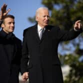 Emmanuel Macron holds Joe Biden's hand as the men wave.