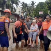 An elderly woman sits on a chair while being carried by coast guard personnel wading through floodwaters in the Philippines.