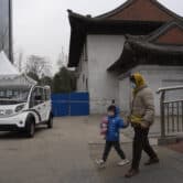 A woman and child wearing masks walk near a closed-off area in Beijing.