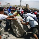 Protesters work together to roll a boulder in Peru.