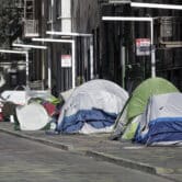 A man stands next to tents on a sidewalk in San Francisco.