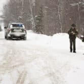 A Vermont State Trooper speaks to a homeowner while snow falls.