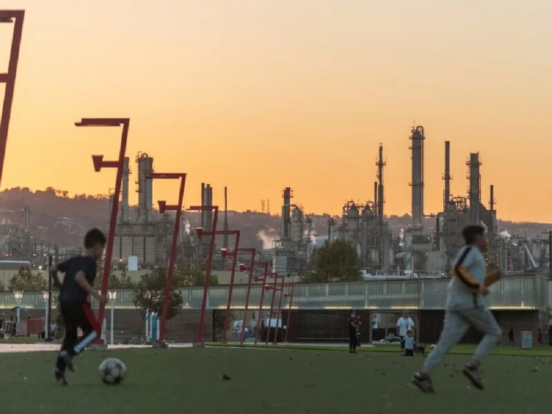 Children playing soccer with an oil refinery in the background.