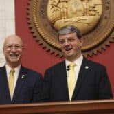Craig Blair and Roger Hanshaw smile while standing in the House chambers at the West Virginia state capitol.