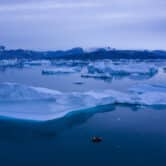 A boat navigates at night next to large icebergs in Greenland.