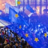 A crowd of protesters is seen through the blue gauze of flags for EU and Ukraine.