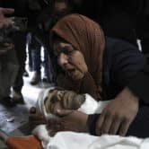 A Palestinian mother surrounded by mourners embraces her son during his funeral.