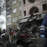 Workers pass the scene where a helicopter crashed on civil infrastructure in Ukraine.