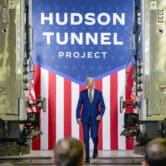 People watch as Joe Biden walks in front of a sign that reads "Hudson Tunnel Project."