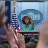 Reporters raise their hands while Karine Jean-Pierre points in their direction during a press conference at the White House.