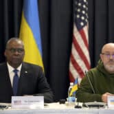 Lloyd Austin and Oleksii Reznikov sit at a table in front of American and Ukrainian flags during a meeting in Germany.