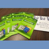 Seven green MoneyPak gift cards lay on a dark brown table next to a white envelope with four stamps at the top and addressed to Sacramento County Superior Court.