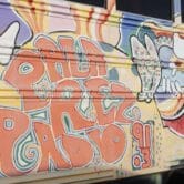 A closeup of a sign on a school bus painted in psychedelic decals and signs that says "Pala Rez Radio."