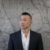 Baimadajie Angwang stands in front of a black and white map of New York City.