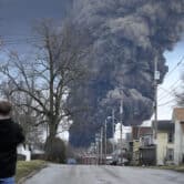 A man takes photos as a black plume rises over East Palestine, Ohio.