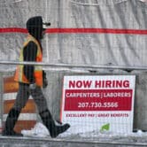 A worker passes a hiring sign at a construction site in Portland, Maine.