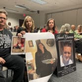 Three women sit in the front row of a House committee meeting holding signs depicting loved ones lost to fentanyl overdoses.