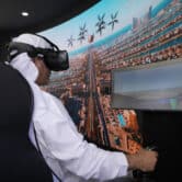 A man sits in a chair while using a virtual reality headset-based flying taxi simulator.