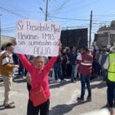An elderly woman in a pink sweatshirt holds a sign with text in Spanish over her head
