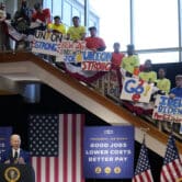Joe Biden gives a speech with union members holding signs on a staircase above him.