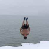 A man jumps into Lake Michigan wearing swim trunks and surf boots during winter.