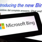A person holds a mobile device displaying the Microsoft Bing logo, in front of a screen displaying additional information about Bing.
