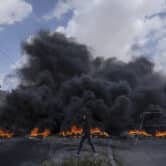 A Palestinian walks past a line of burning tires.