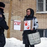 A police officer walks toward a woman holding a poster featuring red hand prints and "STOP."