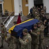Soldiers carry a coffin with a Ukrainian flag draped over it.