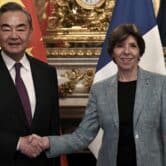 Wang Yi and Catherine Colonna shake hands in front of Chinese and French flags.