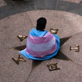 A person wrapped in a transgender pride flag sits at the center of a rotunda