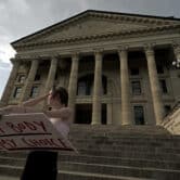 A woman holds a sign reding "MY BODY MY CHOICE" on the steps of the Kansas Statehouse.