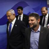 Benjamin Netanyahu and Bezalel Smotrich walk in a hallway, with three people behind them.