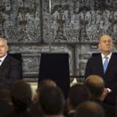Benjamin Netanyahu and Ehud Olmert sit on stage with Israeli flags behind them during a handover ceremony.