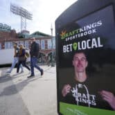 Three people walk by a DraftKings sign featuring Zdeno Chara outside Fenway Park in Boston.