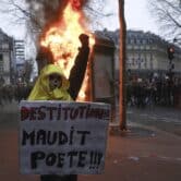 A French protester holds a placard that says "destitution of the cursed poet.”